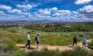 Four hikers, looking over the overspace into the City of Irvine. Sky is blue with big puffy white clouds, on a pretty day.