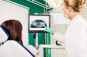 A female dentist points to dental issues on the X-ray displayed on a monitor while explaining results to the patient