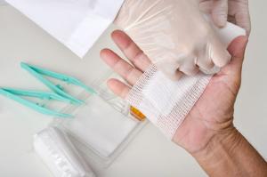 Close-up of wound dressing procedure with bandage being applied to an injured hand.