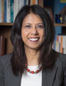 Sharmin Banu, executive coach, in professional attire standing and smiling infront of a bookshelf.