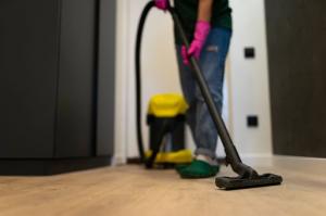 A woman performing water extraction services using a professional vacuum cleaner on a parquet floor in a residential room.