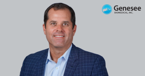 Portrait of Matt Dambeck, Chief Executive Officer of Genesee BioMedical, Inc., wearing a blue checkered blazer in front of a gray background with the company logo.