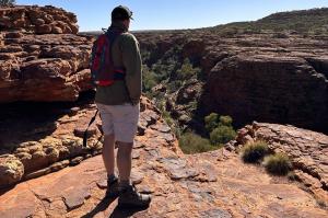 A man stands on a rocky outcrop overlooking a vast red-earth canyon in the Australian outback, symbolizing reflection and journey.
