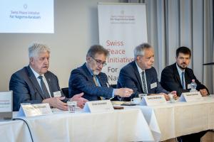Four male speakers sit at a table