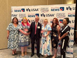 Group photo at the Heroes at Home awards event featuring Eleanor Haack-Finney holding her award, surrounded by fellow honorees and event organizers in front of a branded backdrop.