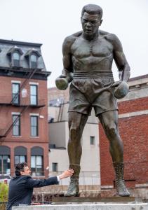 Sculptor Zenos Frudakis reaches out to his statue of Muhammad Ali, the world's largest, at the unveiling ceremony in Lewiston, ME, on May 31, 2025