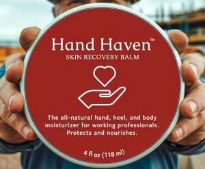 A construction worker’s hands holding a jar of Hand Haven Skin Recovery Balm, featuring a red lid with white text and a heart-hand logo. The label reads "The all-natural hand, heel, and body moisturizer for working professionals. Protects and nourishes. 4