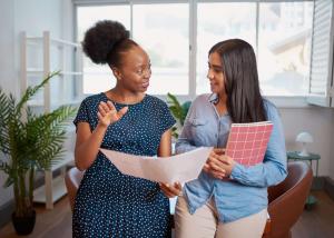 2 ladies reviewing a piece of paper, one mentoring the other and explaining something.