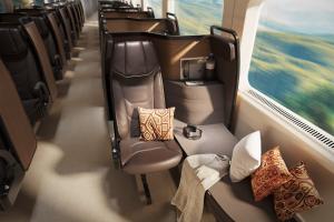 A reclining rail seat next to a wide side couch with pillows, blanket, and headphones arranged for comfort. Window views of rural Quebec blur in motion.