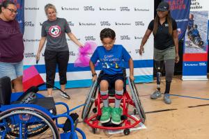 Youth athlete sits in his new basketball chair as three adults congratulate him