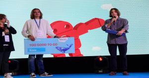  Premiazione durante Maker Faire Rome: un giovane vincitore riceve un assegno simbolico da 3.000 euro per il progetto "Too Good To Go" sul palco del contest MakeITcircular, alla presenza dei presentatori e del pubblico.