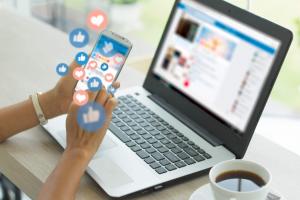 Person scrolling social media on phone, with a laptop in background
