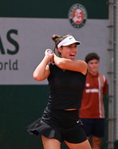 Tennis player Leena Friedman, focused on her backhand. She has brown hair and wears a black tennis outfit.