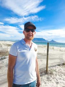 Paul Sartorius standing on the South African coastline in Cape Town, smiling and enjoying the scenic view.