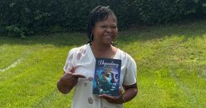 Author Jonnice Cooke smiling and holding her memoir Unpacking the Weight Within while standing outdoors on a sunny day