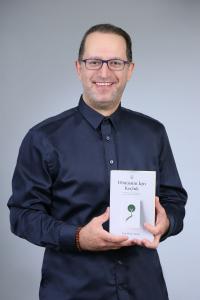 Can Deniz Timur, author of Dönüşüm İçin Koçluk, smiling at the camera and holding his book.