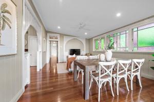 Interior view of an East Brisbane home featuring an open-plan dining and living space with polished timber floors, a rustic timber dining table, white chairs, and stained-glass windows along the side wall.