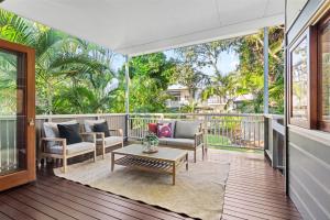 Covered outdoor deck with timber flooring and neutral-toned outdoor lounge setting surrounded by leafy green backyard and palms