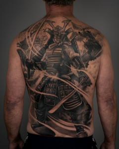 Full back piece in blending Japanese and black and grey realism tattoo styles by Tyler Ciaralanti, featuring a samurai warrior