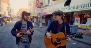 two men strum instruments in image from movie