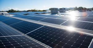 A commercial solar array on a building's flat roof reflects sunlight in several areas on the solar panels.