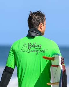 Surfer wearing a green jersey with the ventura county coast logo representing the collaboration with the destination marketing organization and the naval base