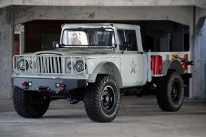 The ANV-KJ1, a restored and modernized Kaiser military Jeep, parked in an industrial-style warehouse garage. The vehicle features rugged tires, military gray paint, and precision-built detailing under soft overhead lighting.