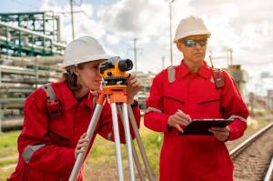 Two engineers in safety vests conduct a custom survey with a leveling instrument at a construction site.
