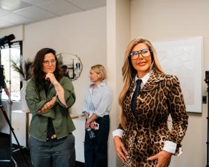 Adriana Gallardo standing in an office wearing a leopard-print suit and tie, surrounded by her production team during a photoshoot.