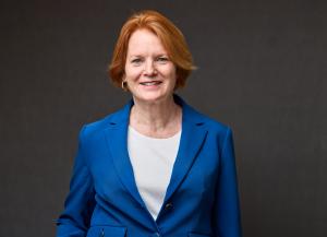 Portrait of Meg Morreale, CFO of Austin Lighthouse for the Blind, wearing a royal blue blazer and white top, smiling in front of a dark gray background