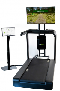 The gaitACTIVE Program is delivered through the GaitBetter system which is an add-on to existing treadmills. The image includes a treadmill, touchscreen on a black stand, the gaitBetter black box system, and a flat screen TV on a stand.