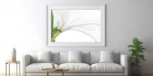  A modern, minimalist living room featuring a sleek white sofa with five matching cushions, centered beneath a large framed photograph of a white lily in close-up. The artwork highlights the soft curves and translucent texture of the flower’s petals, addi