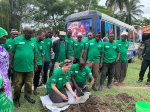 A group of people gather behind two people planting a tree seedling, Mafia Island.