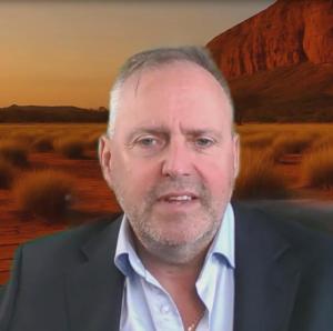 Paul Rushworth-Brown in a collared shirt and jacket, pictured in front of an Australian outback landscape at sunset.