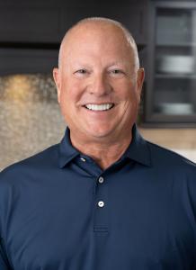 A smiling man with a navy blue polo shirt