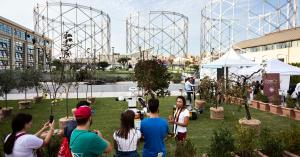 Visitors interact with robotics and agritech prototypes in an outdoor exhibition area at Gazometro Ostiense during Maker Faire Rome, with historic gas holders in the background.