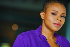 EXCLUSIVE: Award-winning actor Mia Bible is returning to the International Black Film Festival of Nashville (IBFF) for the second consecutive year African-American woman with buzz cut, almond eyes and pink full lips seen from the shoulders up, wearing a purple jacket with blurred background- actor Mia Bible promoting her appearance at the 2025 International Black Film Festival.