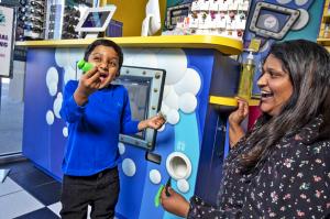 a boy in a blue shirt is jumping up and down with joy as he holds a toy surprise. His mom looks on smiling.
