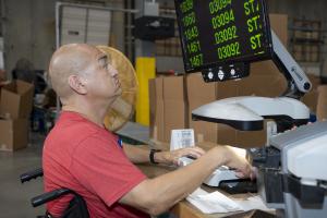 Man using an adaptive magnification device in the Austin Lighthouse for the Blind warehouse to review and process product labels.