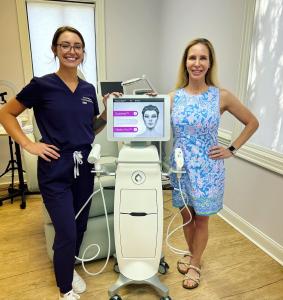 Two women at Concierge Medical Arts standing beside a Candela Matrix Pro device, one in purple scrubs and the other in a blue floral dress, smiling in a treatment room.