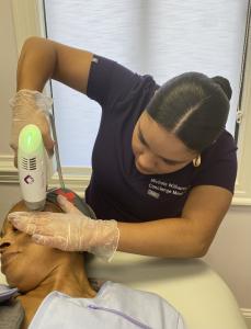 Michele Williams, FICS, of Concierge Medical Arts performing a Candela Matrix Pro skin treatment on a patient’s forehead, wearing gloves and a purple uniform.