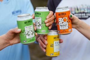 A group of friends doing a cheers with Holidaily cans of gluten-free beer