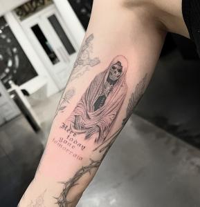 Forearm tattoo of a robed skeleton holding its hands in its lap, with gothic text reading “Here today gone tomorrow.”
