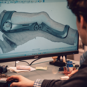 Computer screen displaying a 3D digital model of a custom knee brace, showing detailed contours for a precise patient-specific fit.