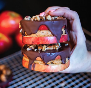 SugarBee® apples sliced and stacked with cookie dough and chocolate over the top being held by a hand