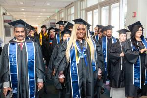 Group of California Intercontinental University graduates in caps and gowns, wearing blue CIU stoles, walking together in a bright hallway during commencement.