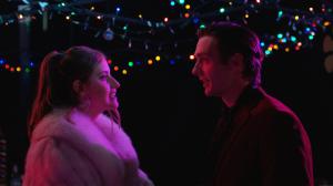 A man and woman smile in front of a colorful background