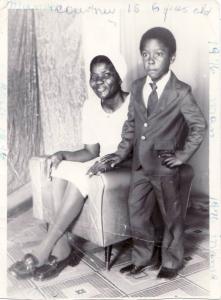 Courtney Williams at age 5 in a suit, standing beside his smiling grandmother in Jamaica.