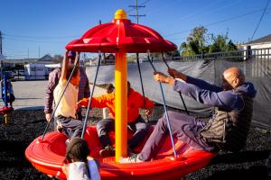 Courtney Williams playing with students on a red spinning playground structure during a school visit.