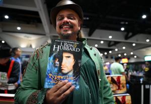 A person dressed as a pirate with headband on is holding a copy of "Typewriter in the Sky" by L. Ron Hubbard while attending the San Diego Comic Con.